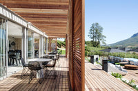 Modern wooden deck with natural tones, sleek gray furniture, and vibrant green landscaping under a clear blue sky.