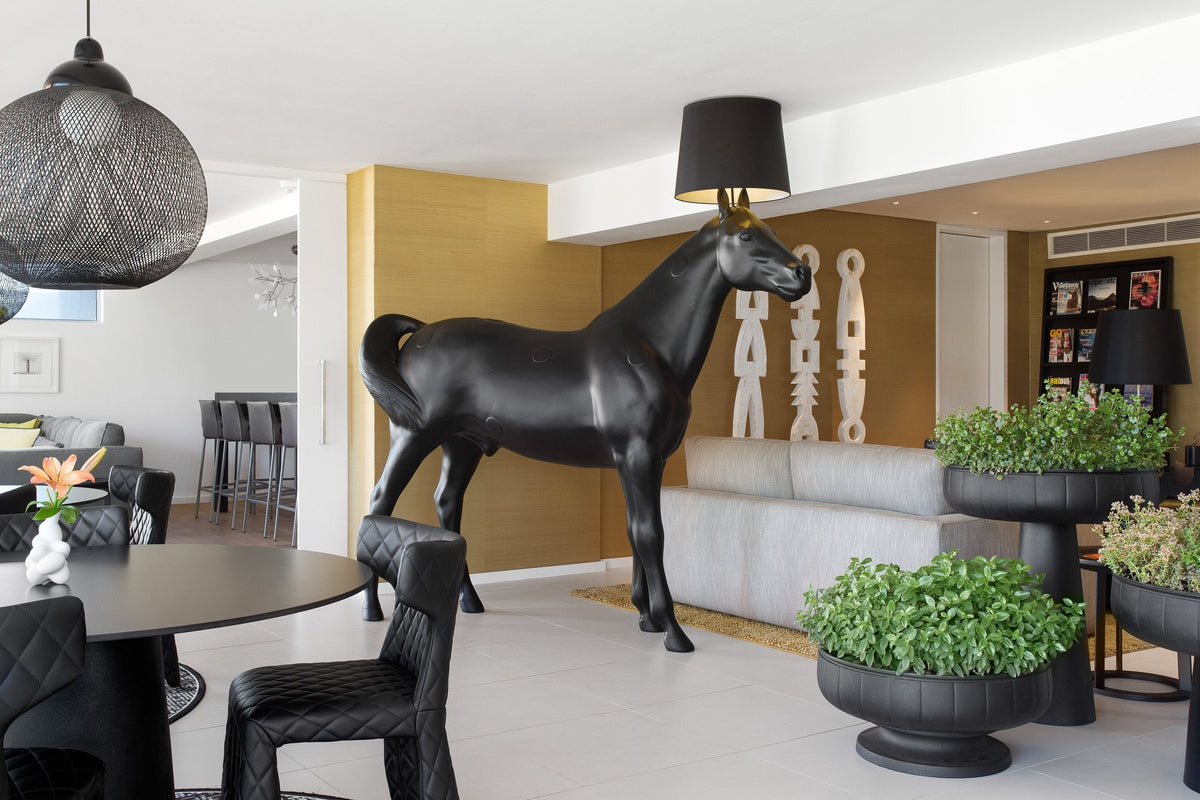 Black horse statue with a lamp, surrounded by modern decor and green plants in elegant indoor setting.