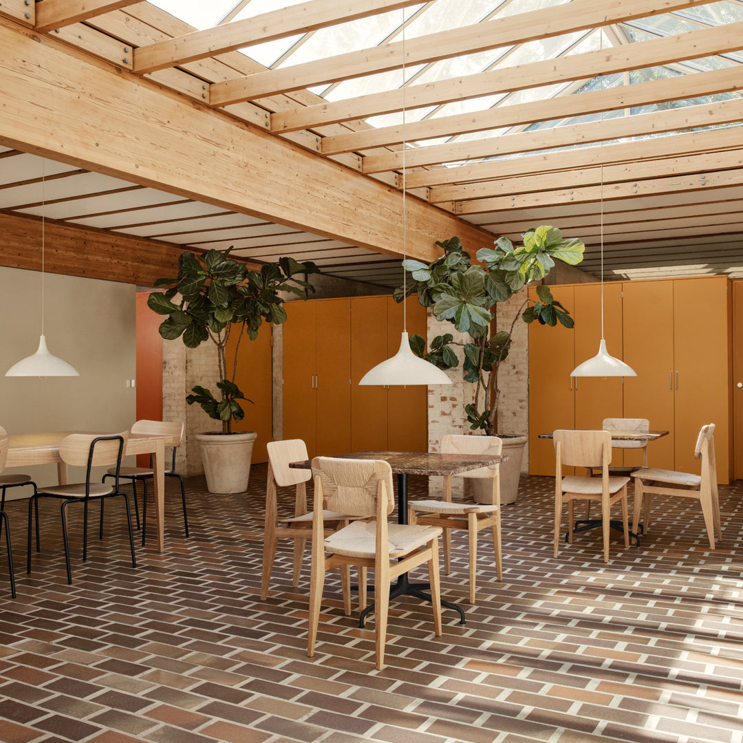 Bright wooden beams, warm orange walls, patterned brown tiles, and lush green plants create a vibrant, cozy indoor atmosphere.