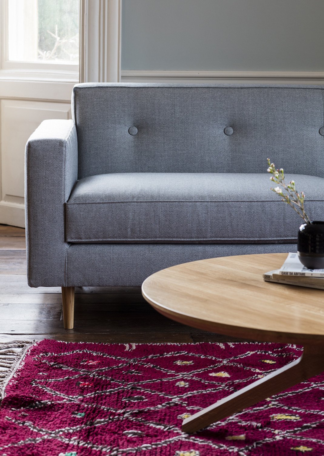 Gray upholstered sofa paired with a round wooden coffee table on a vibrant pink patterned rug.