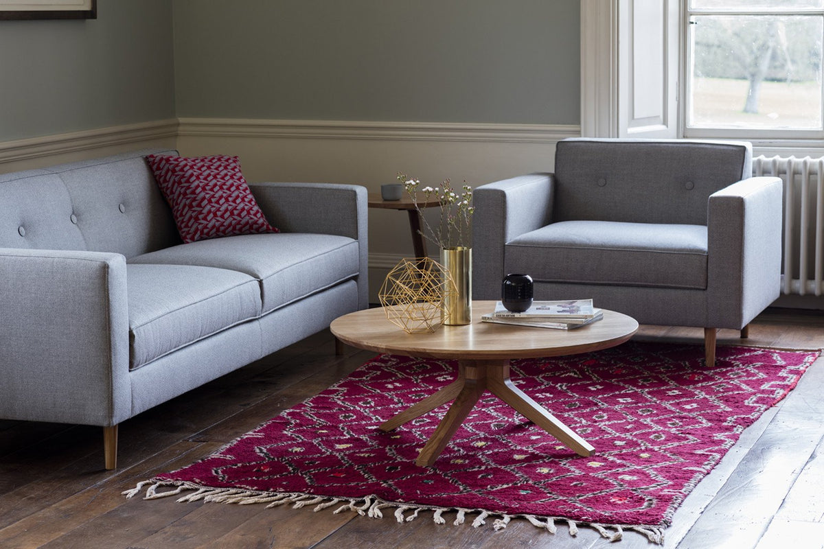 Grey sofa and armchair set with a red patterned rug, featuring intricate designs and a wooden coffee table.