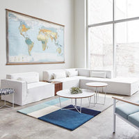 Modern living room featuring white furniture, a blue geometric rug, and a colorful world map on the wall.