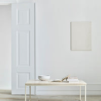 Light grey wall with a minimalistic white table, featuring a simple bowl and books, creating a serene, modern aesthetic.