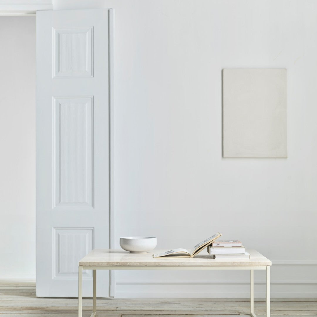 Minimalist white table with a neutral palette, featuring a plain white bowl and stacked books on a light wood floor.