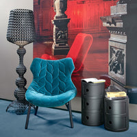 Teal velvet chair with quilted pattern, black cylindrical side tables, and a textured black lamp in a modern decor setting.
