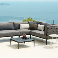Gray sectional outdoor sofa with textured cushions and a modern black table, set against a serene ocean backdrop.