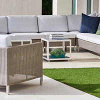 Stylish outdoor seating in light gray with navy accent pillows, featuring a chic woven pattern and a green grass backdrop.