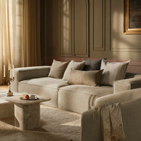 Beige velvet sofa with assorted neutral and earthy-toned cushions, set against a warm, muted color palette.