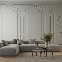 Gray sectional sofa with soft, textured cushions against a light gray wall featuring elegant architectural patterns.