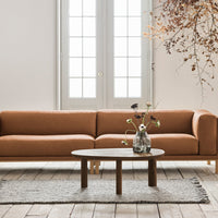Mid-century modern sofa in warm brown fabric, paired with a round wooden coffee table on a soft gray area rug.