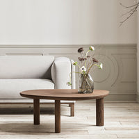 Round wooden coffee table with a rich brown finish, complementing a soft gray sofa in a minimalist setting.