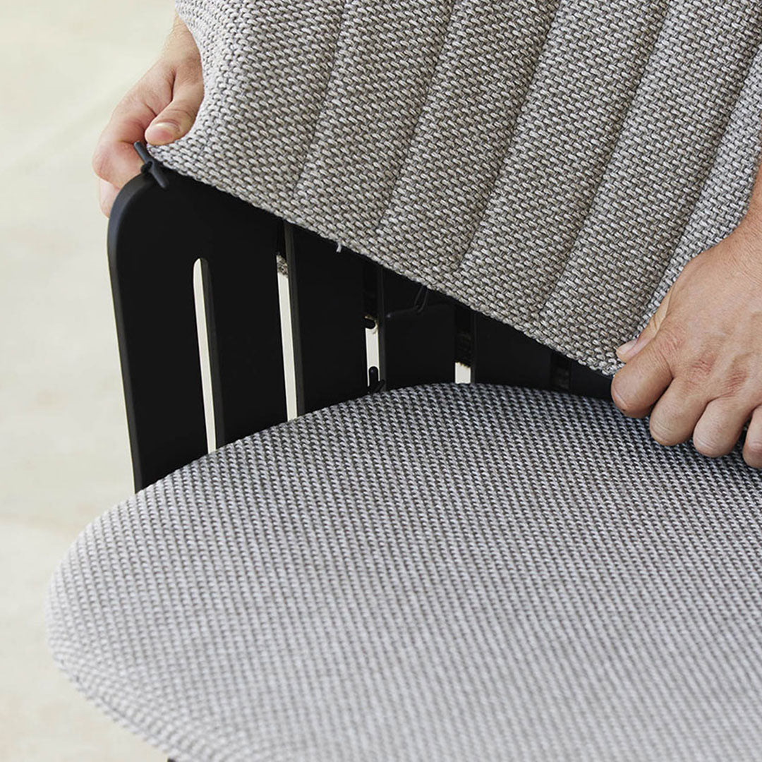 Gray and white striped fabric cushion being adjusted on a black wooden chair.
