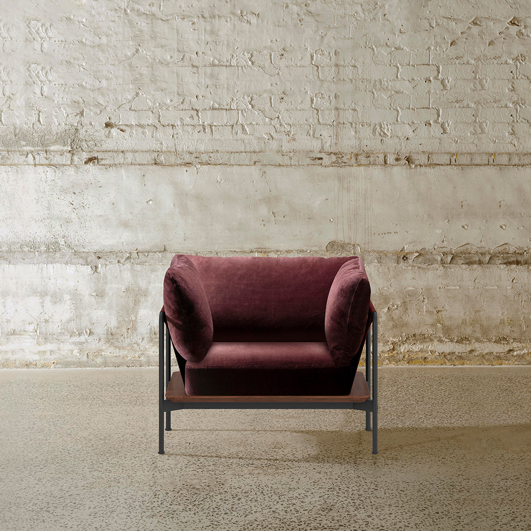Plush maroon armchair with a textured fabric and minimalist black metal frame, set against a rustic wall.