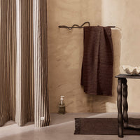 Brown striped towel hanging next to beige striped curtains, complemented by a dark textured rug and black table.