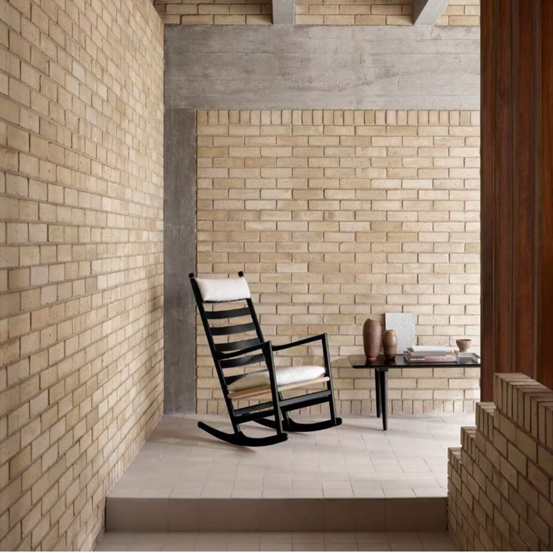 "Vintage black rocking chair with cream cushions against a textured beige brick wall."