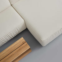 Cream-colored sofa corner with soft textures alongside a natural wood table on a gray floor.