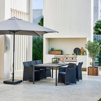 "Stylish outdoor dining set featuring dark wicker chairs, gray umbrella, and minimalist patio decor against neutral background."