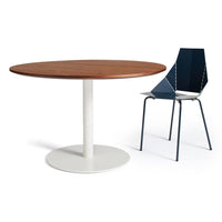 Round wooden dining table with a warm walnut finish and a sleek white base, paired with a modern navy blue chair.