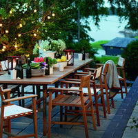"Outdoor dining set with light wood finish, white cushions, colorful floral arrangements, and soft ambient lighting."