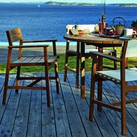 Natural wood tones with white canvas seats, set against a serene blue water backdrop. Outdoor dining furniture.