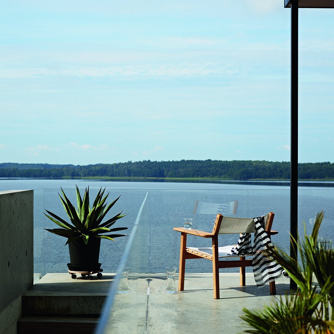 "Relaxing outdoor scene featuring a beige chair, striped black-and-white blanket, and lush green plants against a serene blue backdrop."
