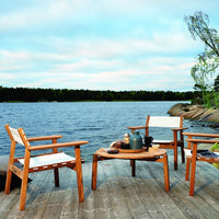 "Light wood outdoor furniture with white cushions, set against a serene lakeside backdrop and soft blue sky."