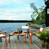 Outdoor scene featuring natural wood tones, white fabric accents, and lush greenery against a serene water backdrop.