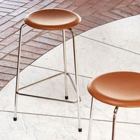 Modern bar stools with sleek chrome legs and warm tan seats, set against a geometric tiled floor.