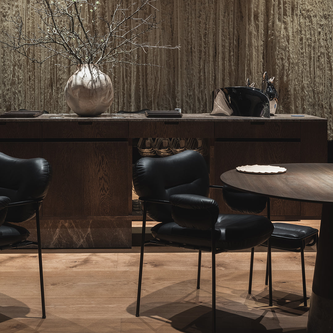 Black upholstered chairs with sleek curves, set against a warm wooden table and rustic-textured background.