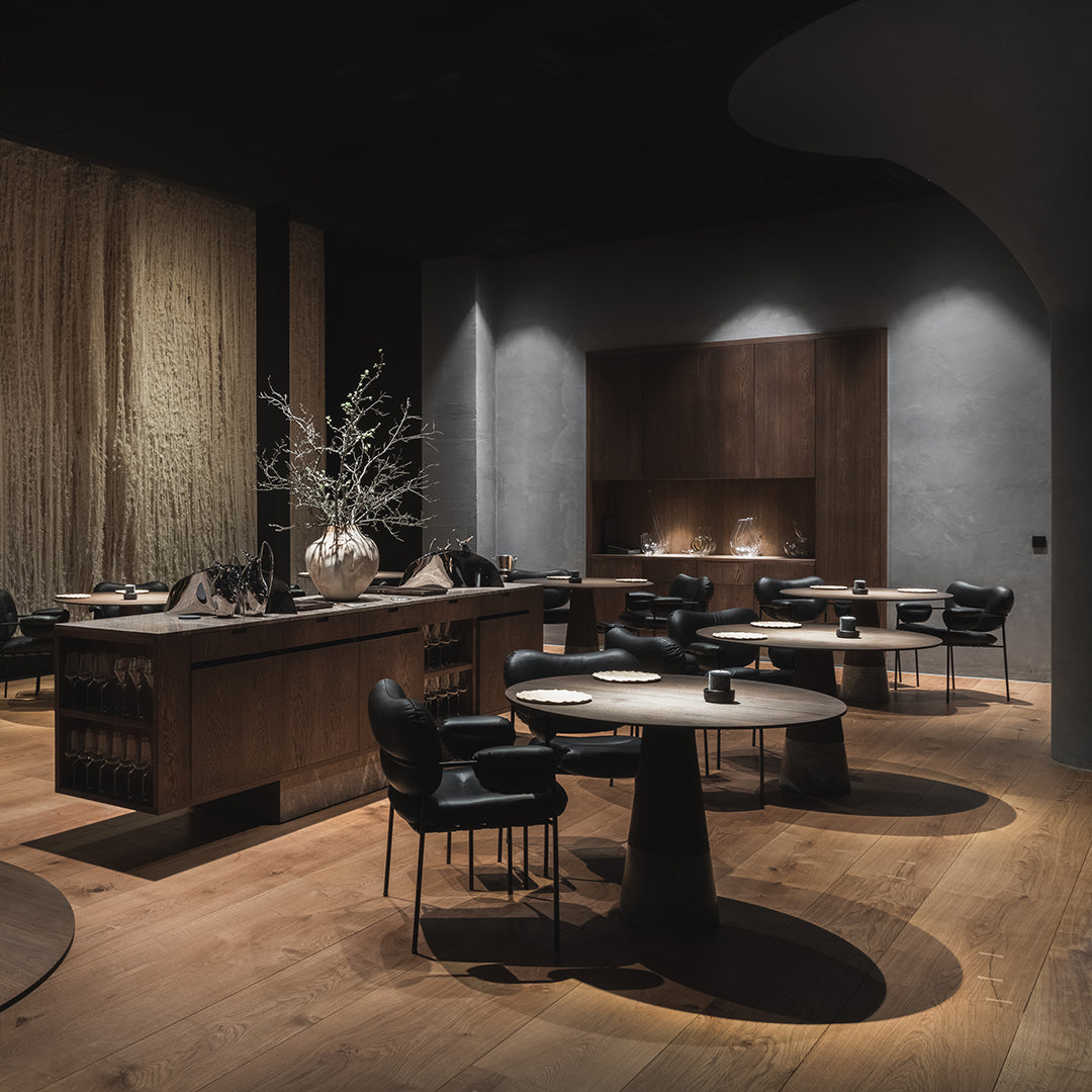 Contemporary dining space with dark wood, black accents, and warm earthy tones. Minimalist design with circular patterns.