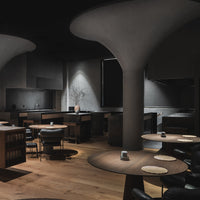 Modern dining space with dark gray walls, wooden flooring, and light wood tables, accented by soft lighting.