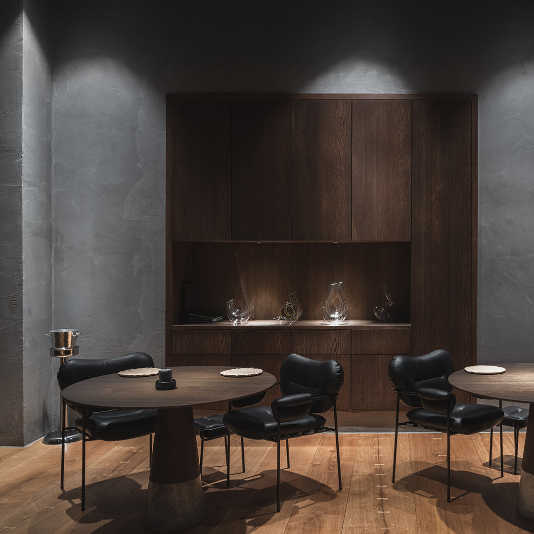 Elegant black chairs and wooden tables contrast with gray walls and warm wood flooring, creating a modern dining atmosphere.