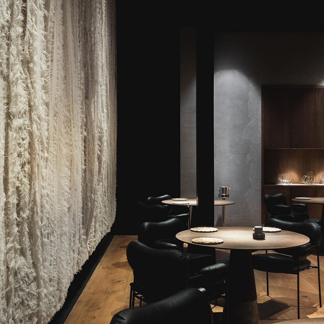 Textured white wall with dark wood accents; elegant black seating around a light wood table in a contemporary setting.