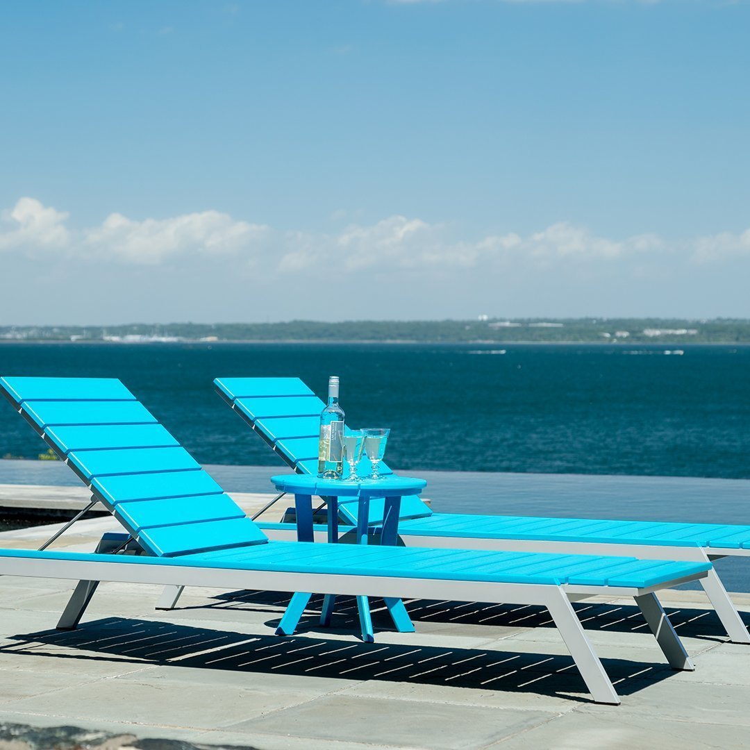 Bright turquoise loungers and table by a pool, set against a serene blue water backdrop and clear sky.