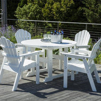 White outdoor dining set with circular table and Adirondack chairs against a natural green backdrop.