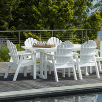 White Adirondack outdoor dining set with a round table and matching chairs, set against lush greenery.