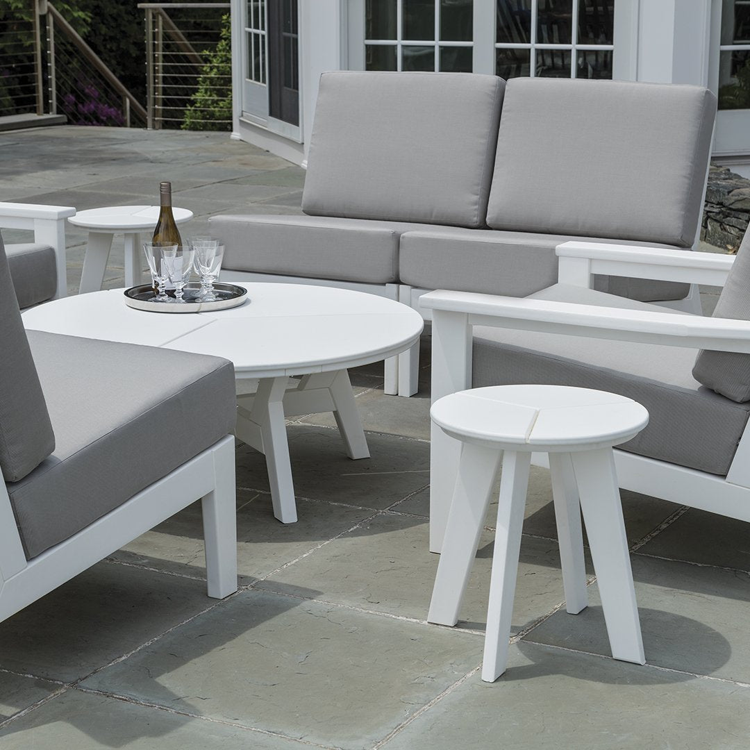 Modern outdoor furniture set featuring white frames with soft gray cushions, circular table, and minimalist design.