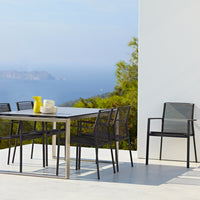 Modern outdoor dining set featuring sleek black metal frames and striped gray chairs against a scenic blue backdrop.
