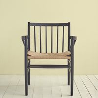 Black wooden chair with a woven beige seat, set against a soft yellow background. Stylish and modern design.