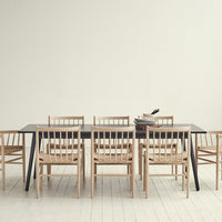"Minimalist wooden dining table with black surface, surrounded by natural wood chairs on a light hardwood floor."