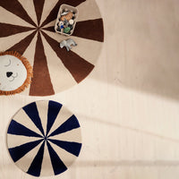 Brown and cream striped rug and navy blue and cream sunburst rug on a light wood floor.