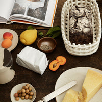 "Neutral tones with rustic textures; features a dark bread, yellow fruits, and earthy dishware against a wooden surface."