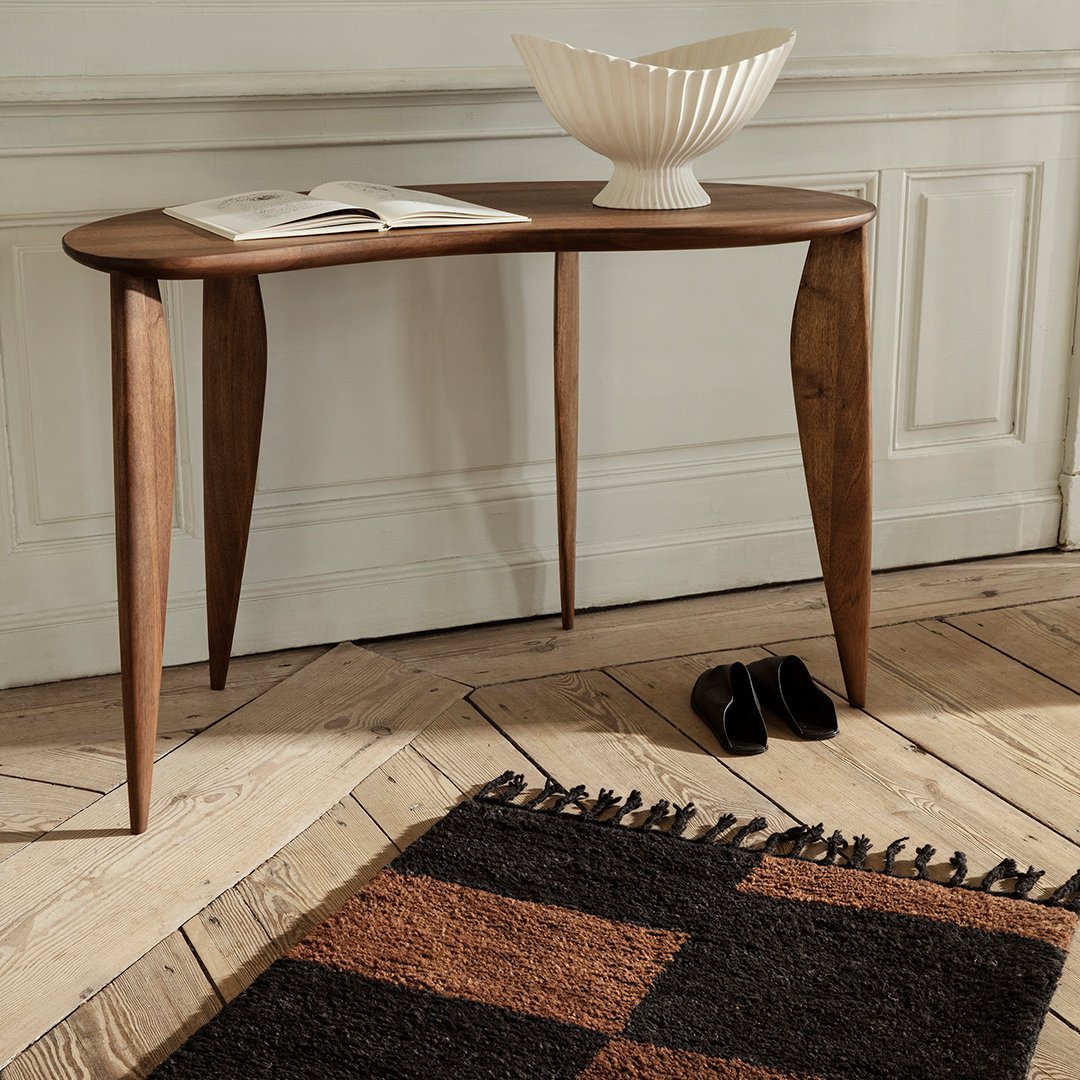 Wooden console table with tapered legs, paired with a geometric brown and black patterned rug. Elegant and modern design.