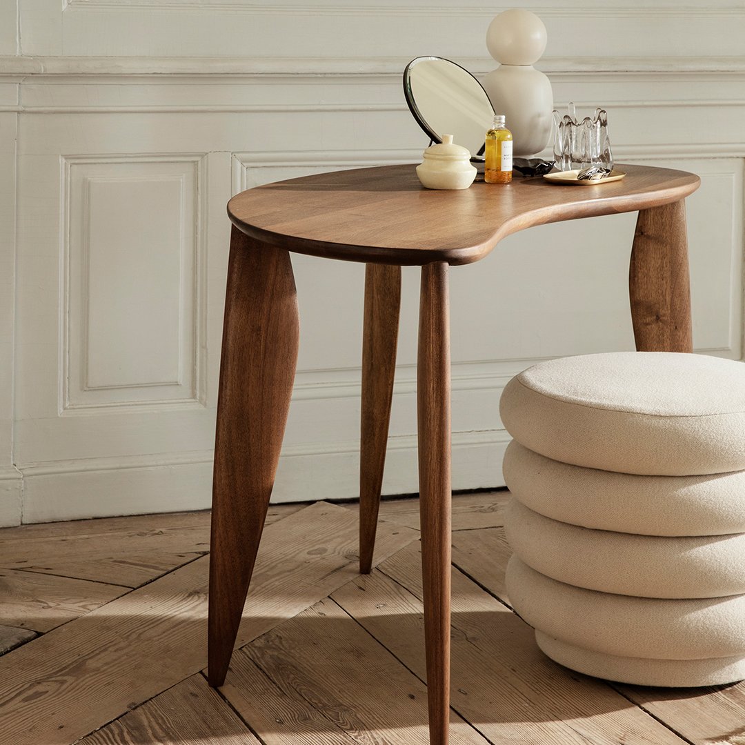 Elegant walnut wood table with smooth, organic curves and tapered legs, paired with a fluffy cream ottoman.