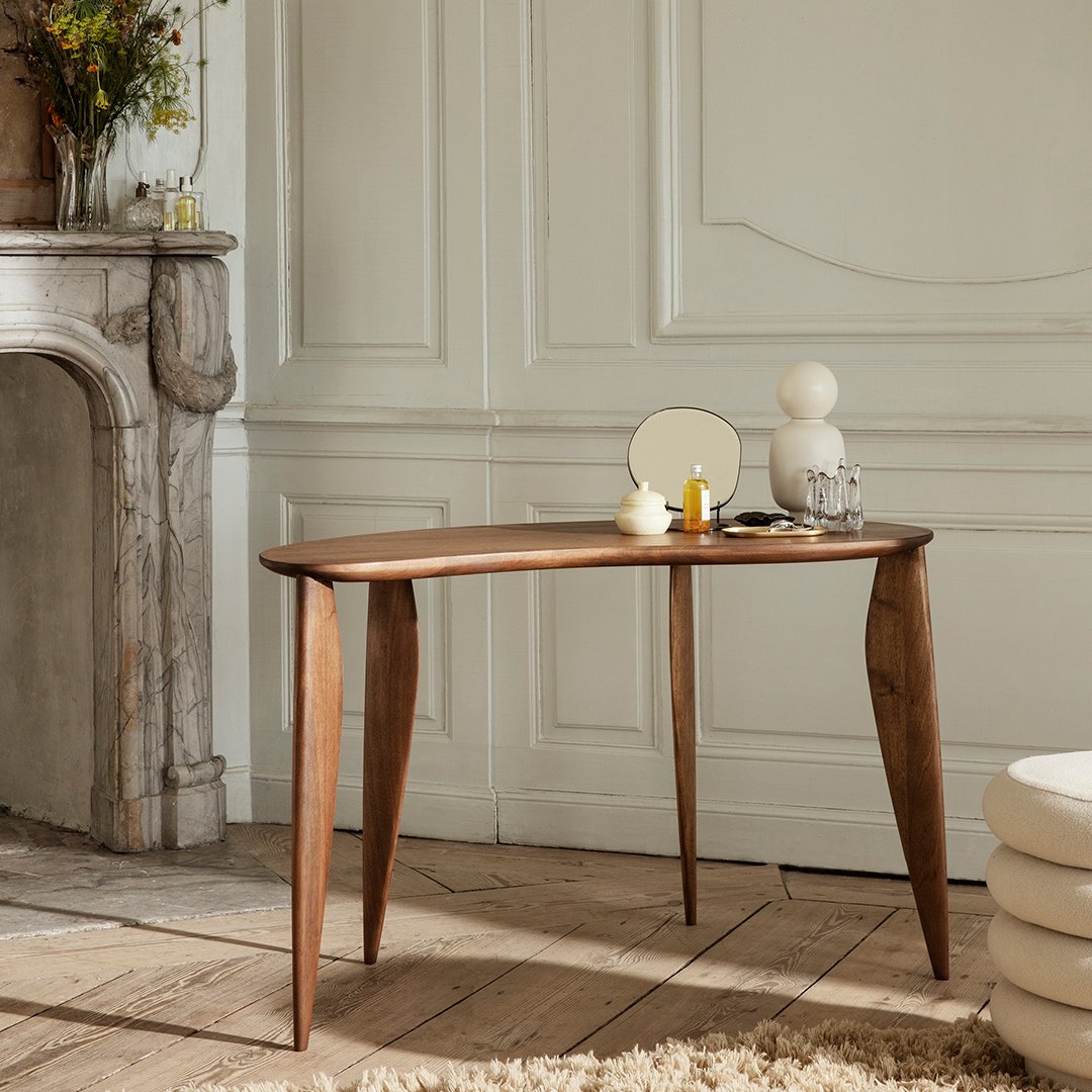 "Curved walnut side table with smooth surface and elegant, tapered legs, set in a bright, neutral room."