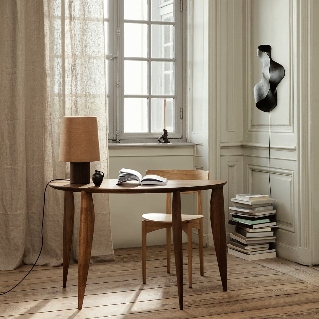 Wooden table with tapered legs, beige lamp, and minimalist decor against light walls and natural wood flooring.