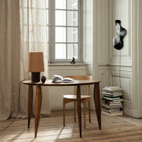 Wooden table with tapered legs, beige lamp, and minimalist decor against light walls and natural wood flooring.