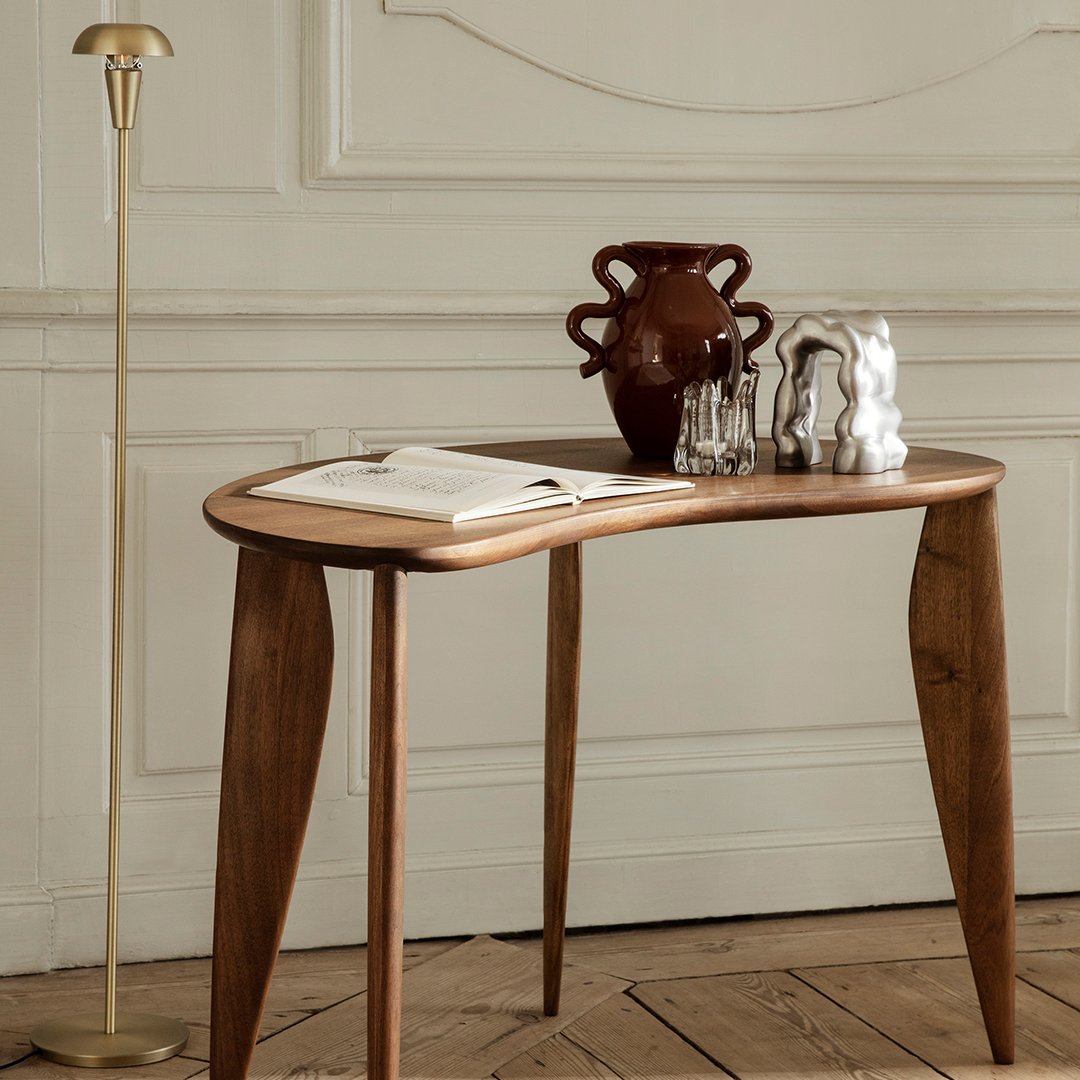 "Elegant wooden table with curved edges, rich brown finish, and minimalist decor against a textured, neutral background."