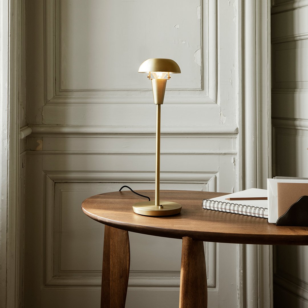 Gold table lamp with a sleek, modern design on a wooden table, featuring a minimalistic base and shade.
