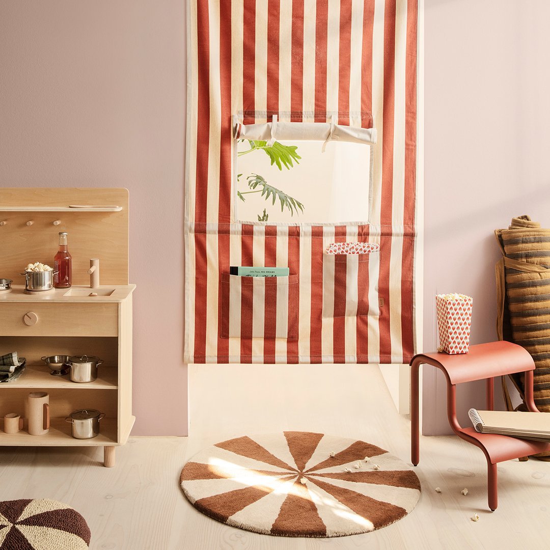 Red and white striped fabric curtain with a round brown and beige patterned rug on a light-colored floor.